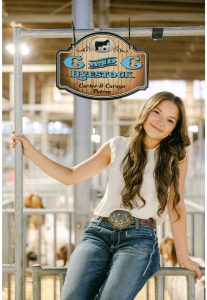 Carsyn Petree smiles and sits on a goat stall.