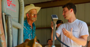 John Miles holds a virtual fencing collar and talks to a cattle producer.