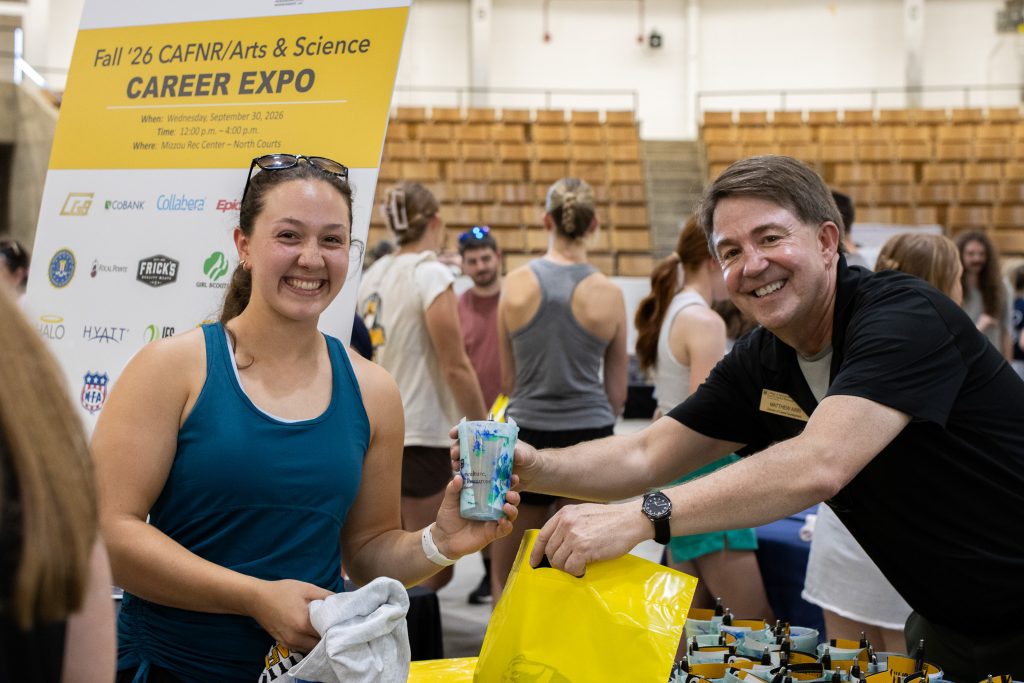Matt Arri and a female student smile while he hands her CAFNR materials.