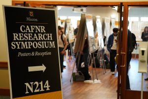 A sign for the CAFNR Research Symposium with people in the background.