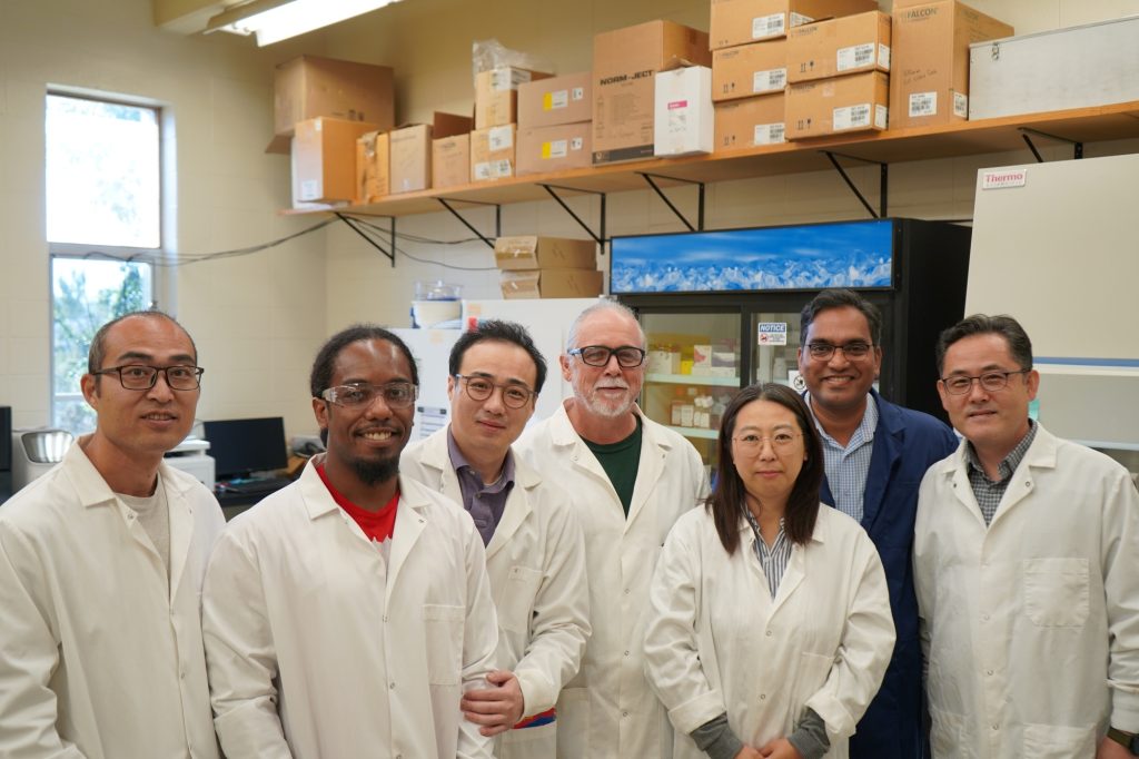Several researchers in lab coats stand in a lab.