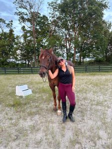 Roselynn Orr stands and smiles next to a horse outdoors.