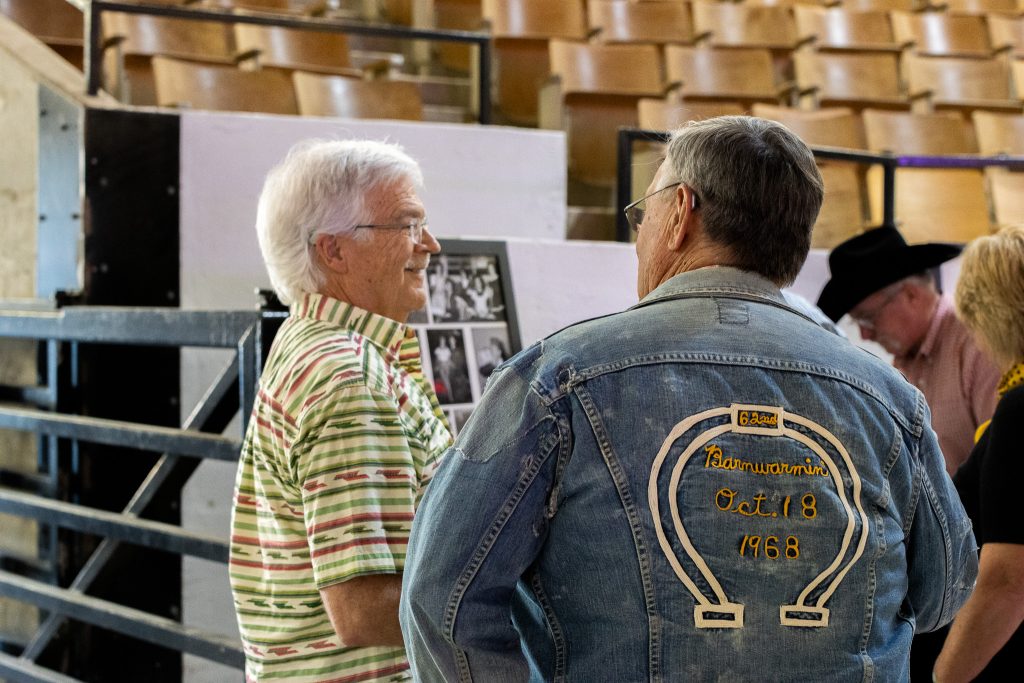 Two men have a conversation inside Trowbridge Arena, one wearing a Barnwarmin' jacket from 1968.